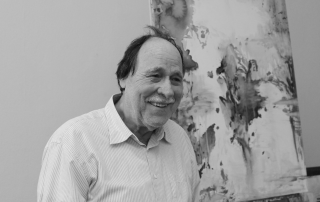 ein Bild in schwarz-weiß. Darauf zu sehen ein Mann der in den Raum lächelt.