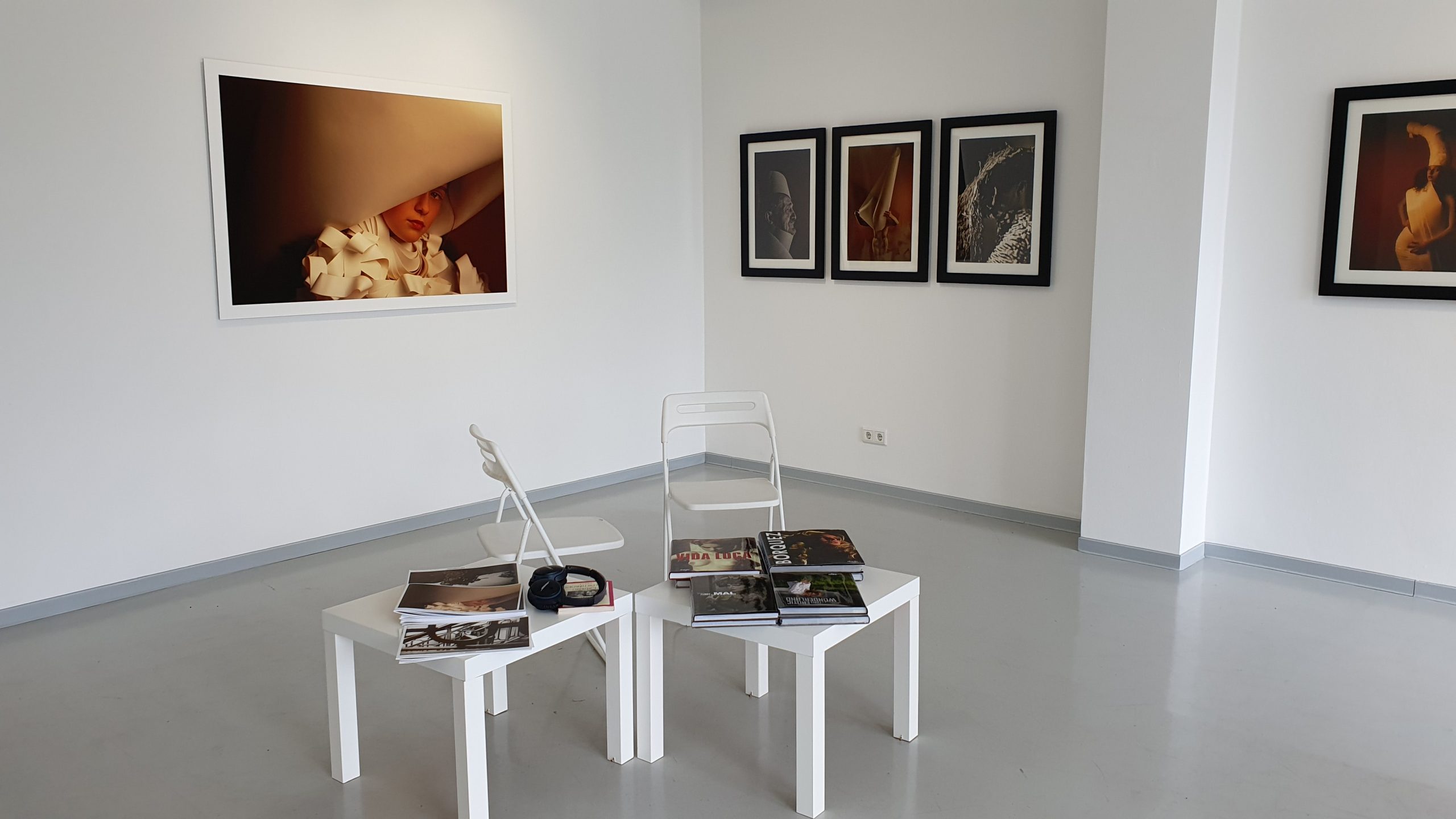 Wand mit verschiedenen Fotografien in einem Raum mit zwei kleinen Tischen und Stühlen.